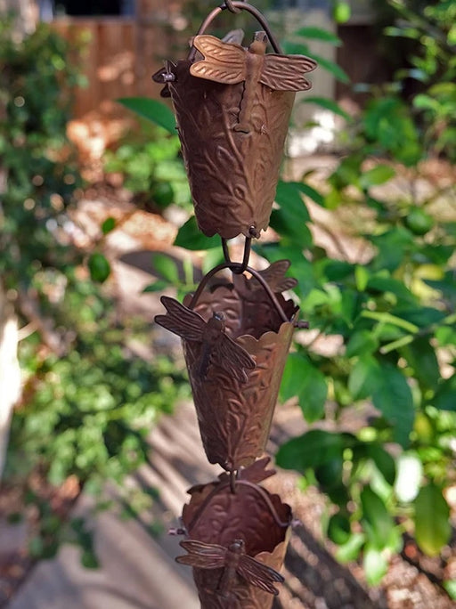Dragonfly copper rain chain with hand-tooled floral cups in a tropical garden